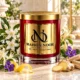 Red MAISON NOOR candle with gold lid beside jasmine, honeysuckle, violets, lemon peel, ginger and pale wood on ivory stone.