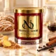 Red MAISON NOOR candle with gold lid beside iced gingersnap cookies, ginger, brown sugar, vanilla, cinnamon and cloves, with milk and molasses behind.