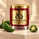 Red MAISON NOOR candle with gold lid on ivory stone beside fresh green jalapeno peppers and a sliced jalapeno.