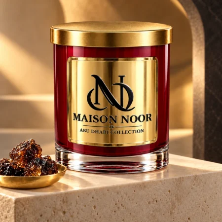 Red MAISON NOOR candle with gold lid on ivory stone beside dark labdanum resin in a shallow gold dish under warm light.