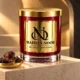 Red MAISON NOOR candle with gold lid on ivory stone beside dark labdanum resin in a shallow gold dish under warm light.