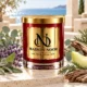 Red MAISON NOOR candle with gold lid beside lavender, sage, eucalyptus, honeydew melon, cypress and weathered wood overlooking the sea.