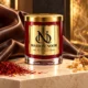 Red MAISON NOOR candle with gold lid on ivory stone beside saffron and incense resin, with rich brown leather draped behind.