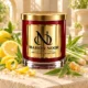 Red MAISON NOOR candle with gold lid beside lemon, peel curls, lemon verbena leaves, lemongrass, sugar and benzoin resin on ivory stone.