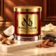 Red MAISON NOOR candle with gold lid beside almonds, coconut, shea butter, tonka beans and wood on ivory stone in a warm wood-paneled salon.