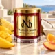 Red MAISON NOOR candle with gold lid beside mango, pineapple, orange, peach, coconut and coconut milk on ivory stone overlooking the sea.