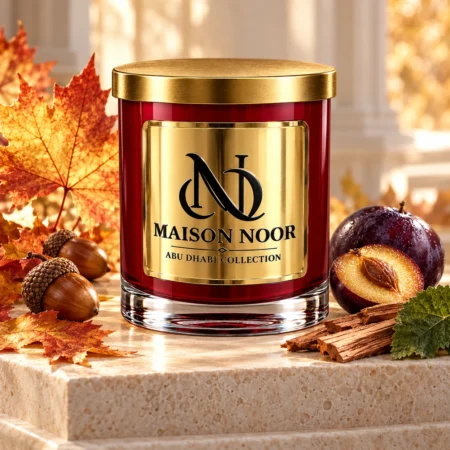 Red MAISON NOOR candle with gold lid beside autumn maple leaves, acorns, plum, patchouli leaf and sandalwood on ivory stone.