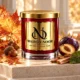 Red MAISON NOOR candle with gold lid beside autumn maple leaves, acorns, plum, patchouli leaf and sandalwood on ivory stone.