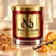 Red MAISON NOOR candle with gold lid beside brown sugar, maple syrup, citrus peel and vanilla on ivory stone.