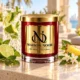 Red MAISON NOOR candle with gold lid beside lime, mint, pineapple and jasmine, with a crystal mojito glass in a coastal setting.