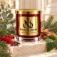 Red MAISON NOOR candle with gold lid beside eucalyptus, pine, fir, red currants, cloves, patchouli leaf and cedar wood on ivory stone.