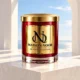 MAISON NOOR Ozonic Element red and gold candle on an ivory stone plinth in a bright open pavilion overlooking a blue horizon.